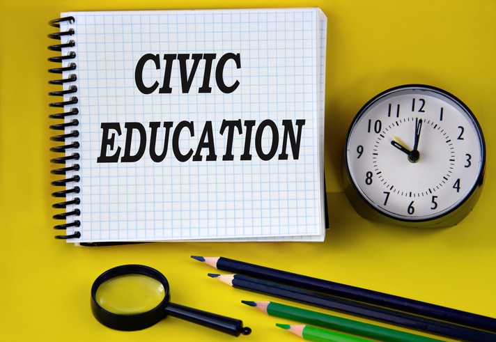 CIVIC EDUCATION - words in a white notebook with an alarm clock, pencils and magnifying glass in the background